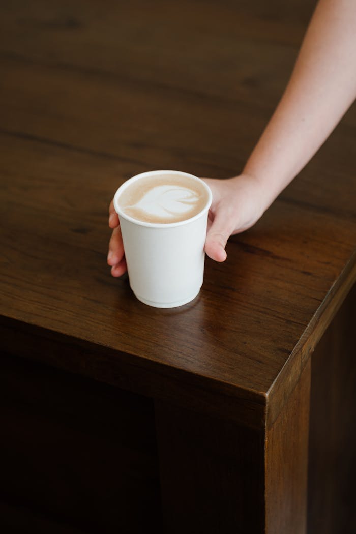 digital From above of unrecognizable female bartender putting paper cup with delicious latte to go on wooden counter while working in modern coffee house